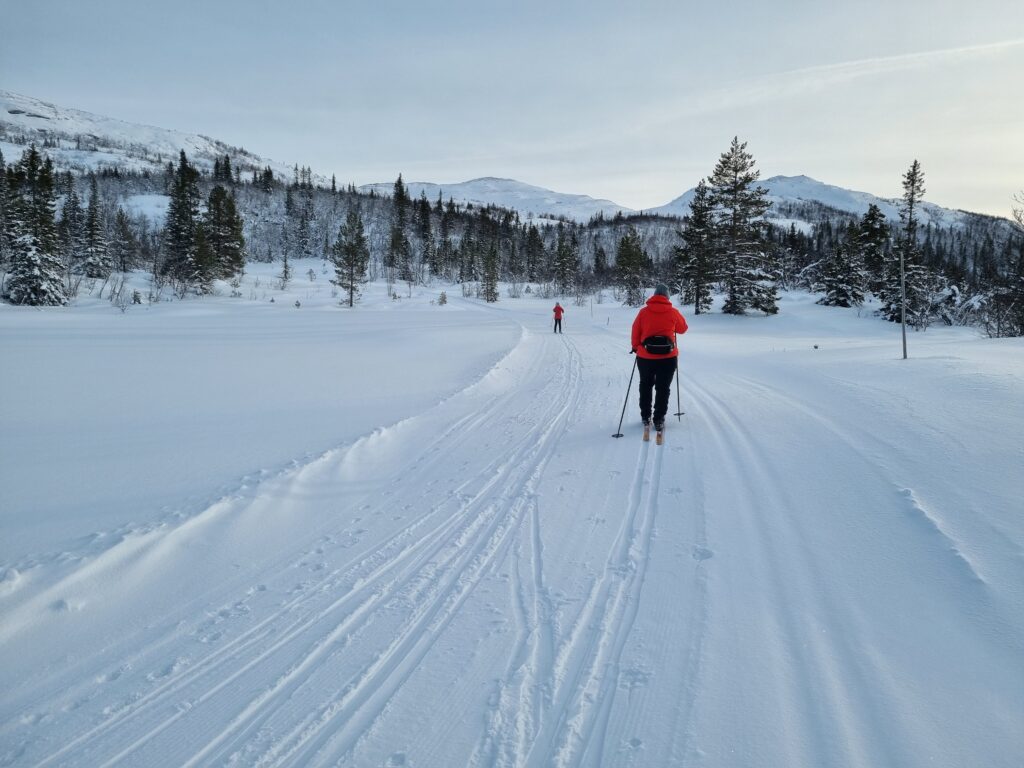 To skigåere med røde jakker kommer imot hverandre i en bred skitrasé med flere spor.